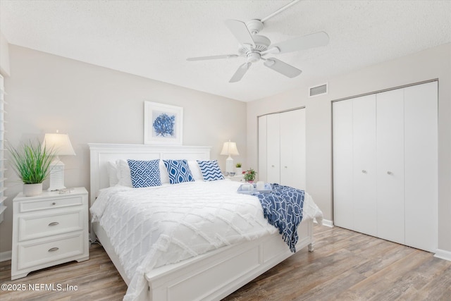 bedroom with ceiling fan, light hardwood / wood-style floors, a textured ceiling, and multiple closets