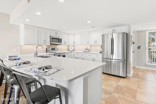 kitchen featuring white cabinetry, sink, stainless steel appliances, kitchen peninsula, and a kitchen bar