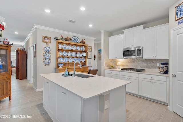 kitchen featuring a kitchen island with sink, white cabinets, black gas stovetop, sink, and decorative backsplash