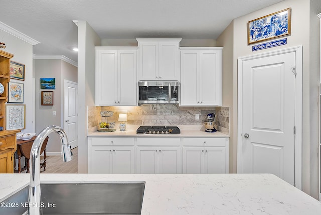 kitchen featuring sink, backsplash, black gas stovetop, white cabinets, and ornamental molding