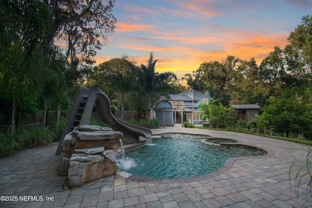 pool at dusk featuring an in ground hot tub, pool water feature, a patio area, and a water slide