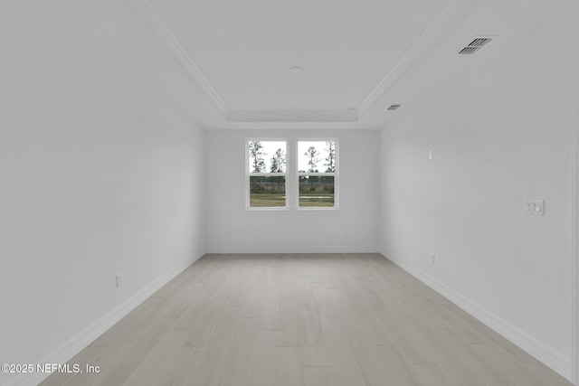 empty room featuring a raised ceiling, visible vents, light wood finished floors, and ornamental molding