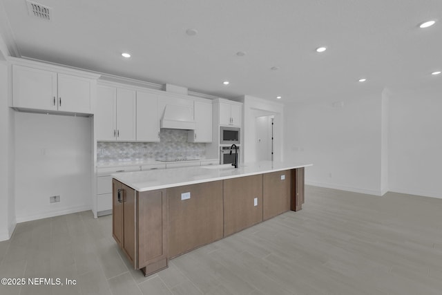 kitchen with visible vents, a sink, stainless steel microwave, white cabinets, and a large island with sink