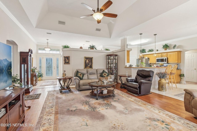 living room featuring ornamental molding, a raised ceiling, ceiling fan, and light wood-type flooring