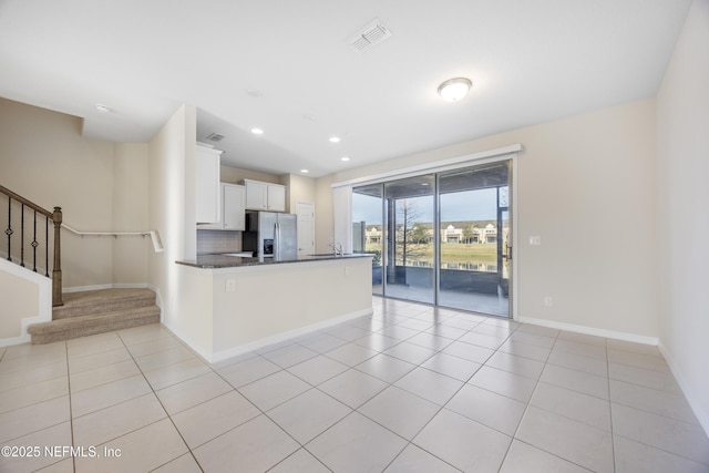 kitchen with white cabinets, stainless steel refrigerator with ice dispenser, tasteful backsplash, light tile patterned flooring, and kitchen peninsula