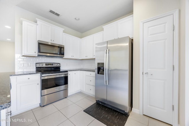 kitchen with backsplash, white cabinets, dark stone countertops, light tile patterned floors, and appliances with stainless steel finishes