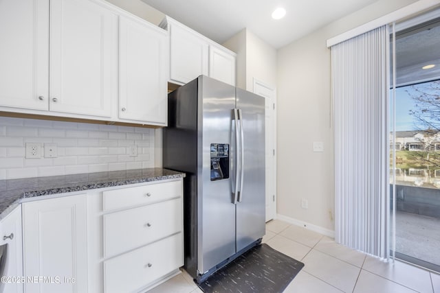 kitchen featuring tasteful backsplash, dark stone countertops, white cabinets, stainless steel fridge with ice dispenser, and light tile patterned flooring