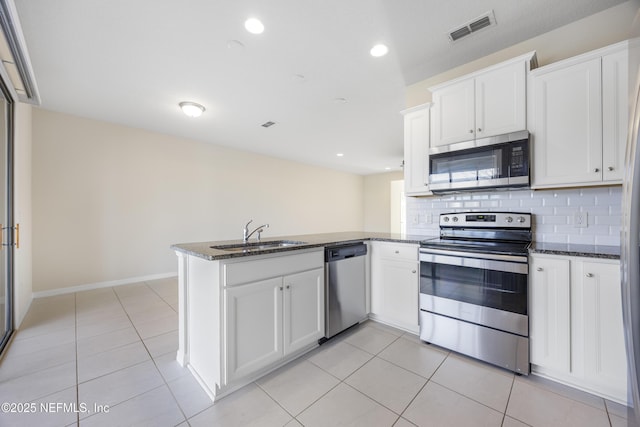 kitchen featuring kitchen peninsula, appliances with stainless steel finishes, dark stone counters, and sink