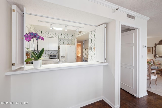 interior space with dark parquet flooring, a textured ceiling, crown molding, white cabinets, and white fridge with ice dispenser