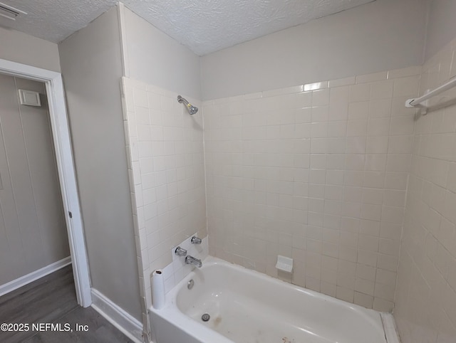 bathroom featuring a textured ceiling, tiled shower / bath combo, and wood-type flooring