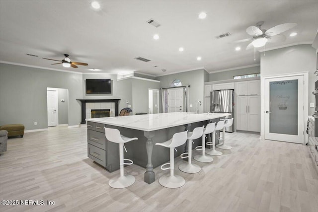 kitchen with gray cabinetry, a large island, light stone countertops, stainless steel fridge with ice dispenser, and a kitchen bar