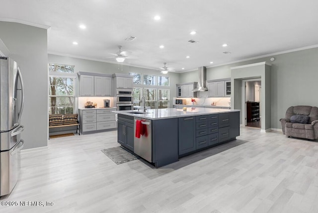 kitchen with a center island with sink, sink, light hardwood / wood-style flooring, wall chimney exhaust hood, and appliances with stainless steel finishes