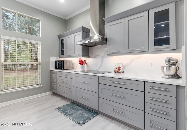 kitchen featuring decorative backsplash, ornamental molding, gray cabinetry, black appliances, and wall chimney range hood