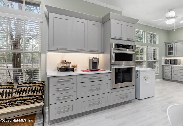 kitchen with ceiling fan, double oven, ornamental molding, and gray cabinetry