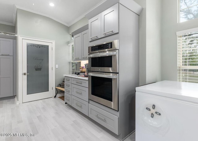 kitchen featuring crown molding, gray cabinets, tasteful backsplash, light hardwood / wood-style floors, and stainless steel double oven