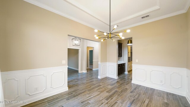 empty room featuring a raised ceiling, wood-type flooring, crown molding, and an inviting chandelier