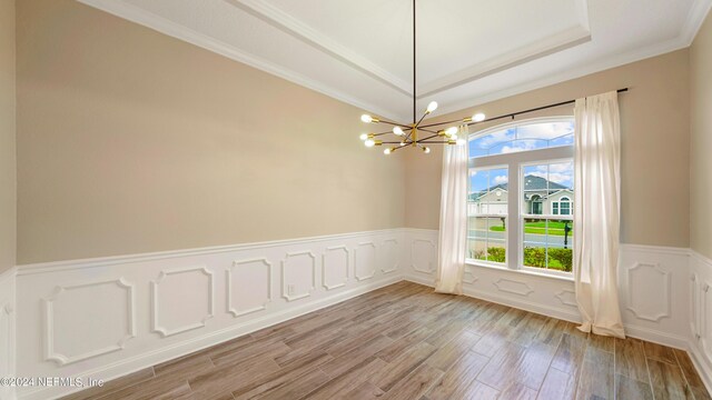 empty room with a raised ceiling, light hardwood / wood-style flooring, an inviting chandelier, and crown molding