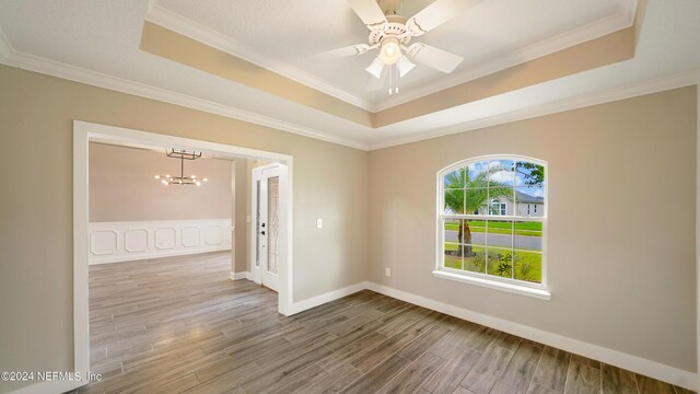 empty room featuring ceiling fan with notable chandelier, crown molding, and a tray ceiling