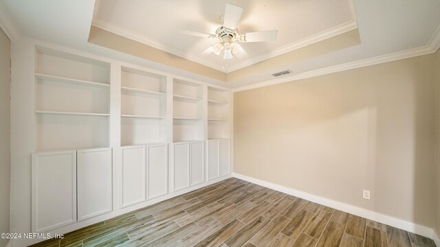 spare room with a tray ceiling, built in features, ceiling fan, and ornamental molding