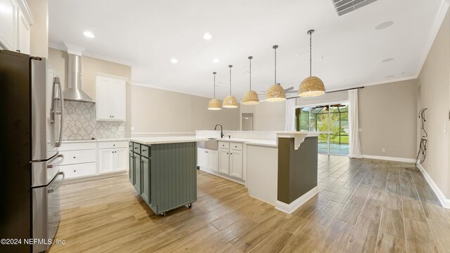 kitchen featuring a kitchen island with sink, wall chimney exhaust hood, stainless steel fridge, tasteful backsplash, and decorative light fixtures