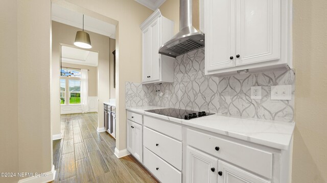 kitchen with black electric stovetop, crown molding, wall chimney range hood, light hardwood / wood-style flooring, and white cabinets