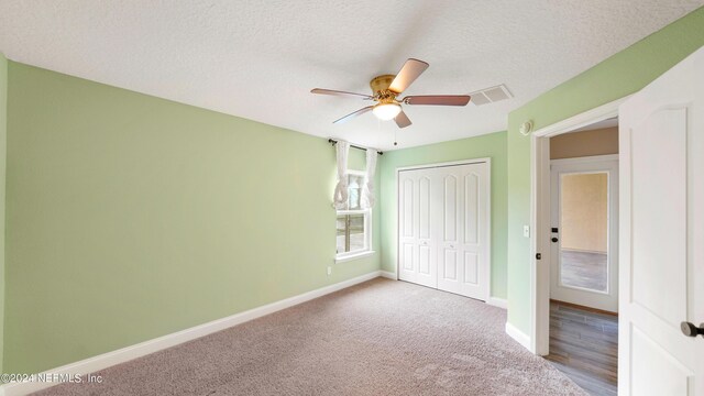 unfurnished bedroom with a textured ceiling, a closet, ceiling fan, and carpet floors