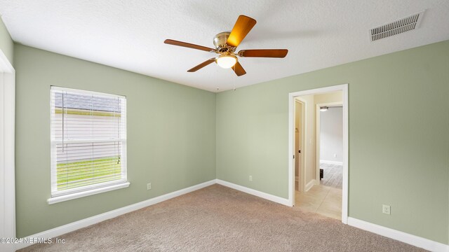 spare room featuring a textured ceiling, light colored carpet, plenty of natural light, and ceiling fan