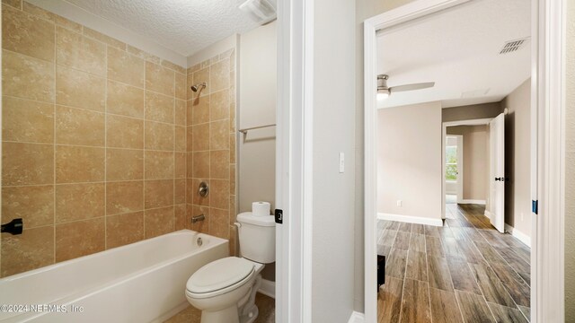 bathroom featuring ceiling fan, toilet, a textured ceiling, and tiled shower / bath