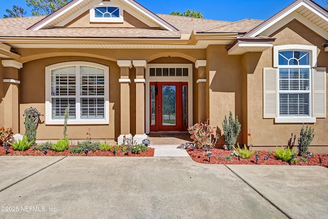 view of exterior entry featuring roof with shingles and stucco siding