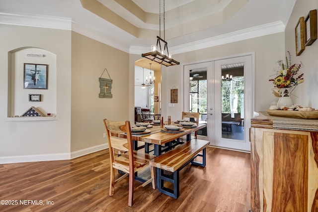 dining room with baseboards, a raised ceiling, wood finished floors, crown molding, and french doors