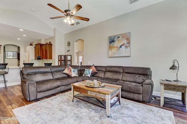 living room featuring arched walkways, ceiling fan, lofted ceiling, wood finished floors, and baseboards