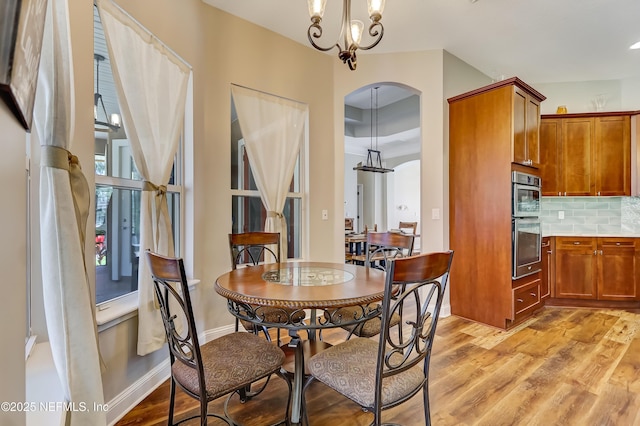 dining room featuring light wood-style floors, arched walkways, a notable chandelier, and baseboards