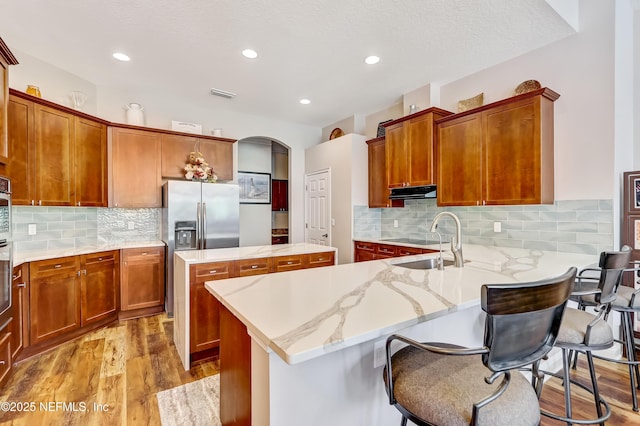 kitchen featuring visible vents, a kitchen island, a sink, wood finished floors, and under cabinet range hood