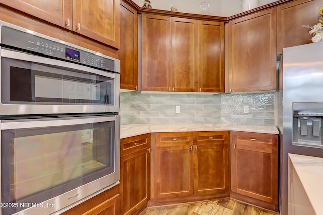 kitchen featuring light countertops, appliances with stainless steel finishes, brown cabinetry, and tasteful backsplash