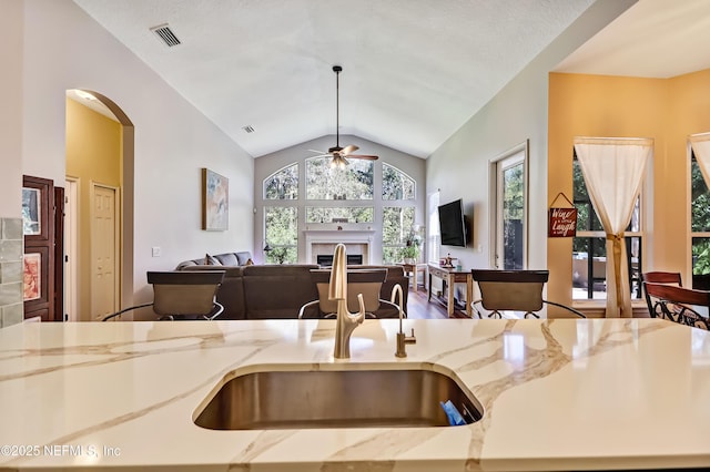 kitchen featuring lofted ceiling, light stone counters, a fireplace, visible vents, and open floor plan