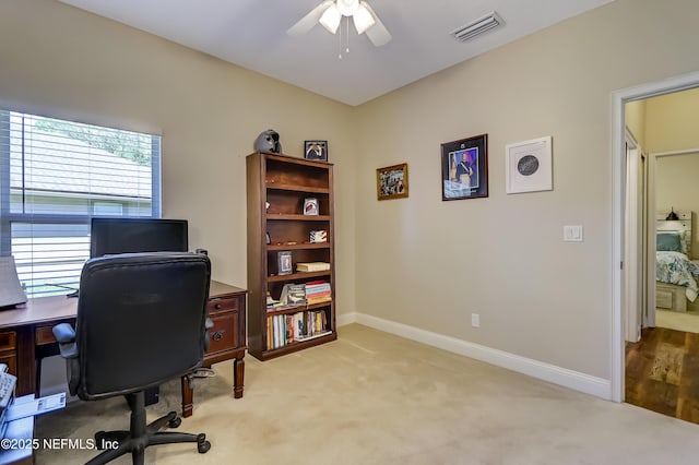 office space with a ceiling fan, light colored carpet, visible vents, and baseboards