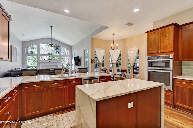 kitchen featuring a fireplace, stainless steel appliances, open floor plan, a sink, and ceiling fan with notable chandelier