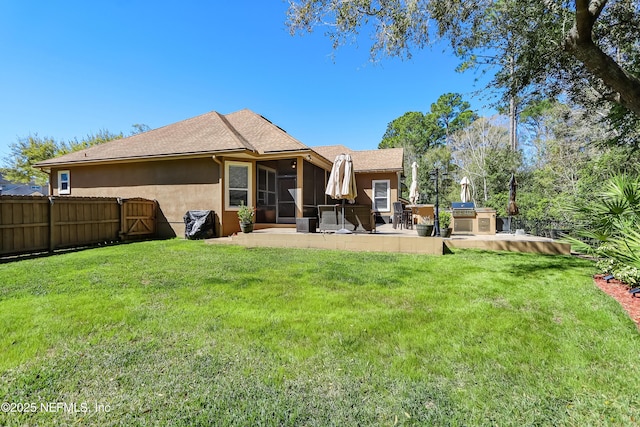 back of property featuring a yard, a patio, stucco siding, a sunroom, and fence