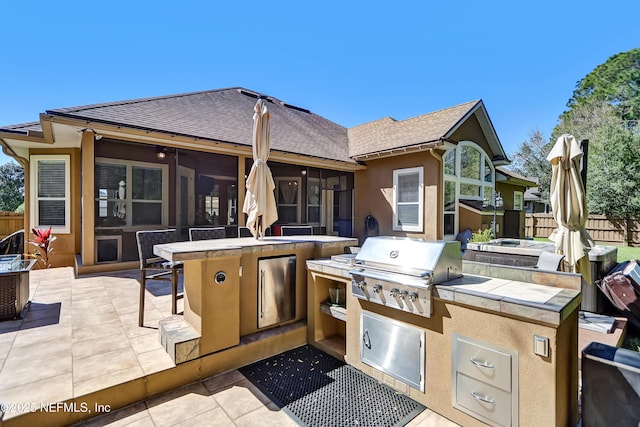 view of patio featuring a sunroom, fence, an outdoor kitchen, and area for grilling