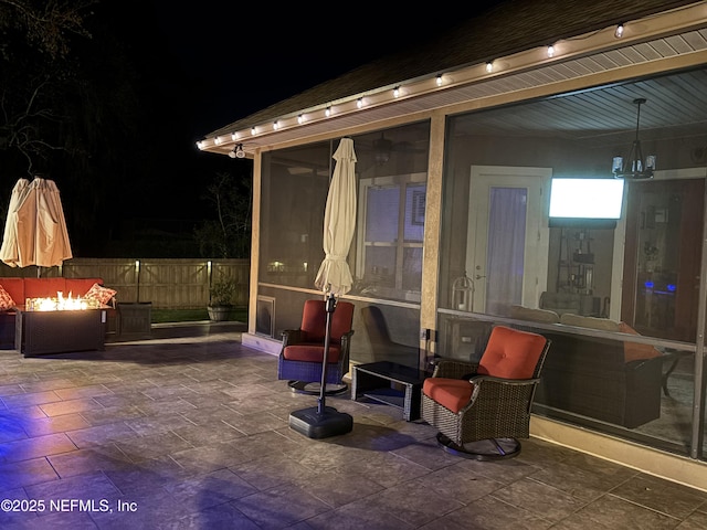 patio at twilight with a fire pit, fence, and a sunroom