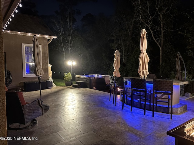 patio at night with a hot tub and outdoor dining area