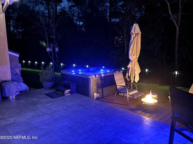 patio at twilight with an outdoor fire pit, fence, and a hot tub