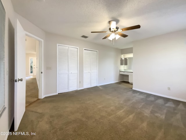 unfurnished bedroom with dark carpet, a textured ceiling, ceiling fan, connected bathroom, and multiple closets