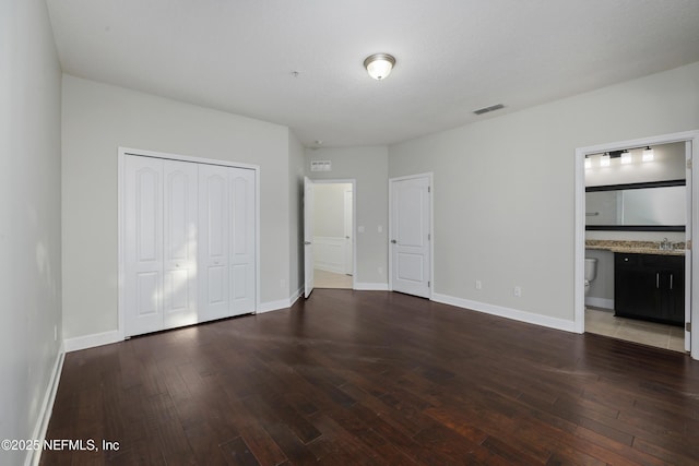 unfurnished bedroom with ensuite bathroom and dark hardwood / wood-style floors