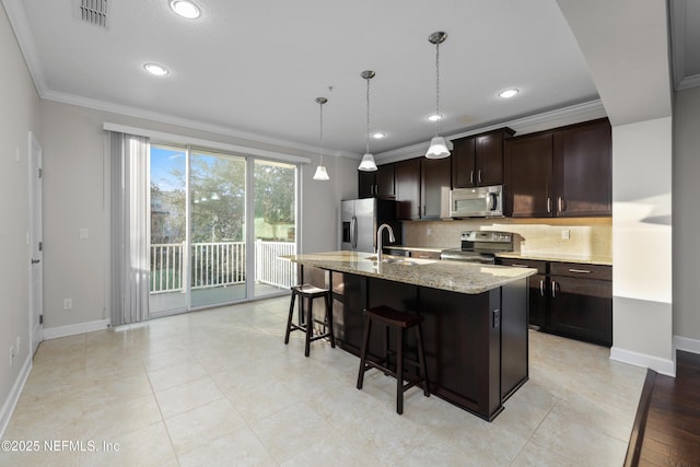 kitchen featuring light stone countertops, appliances with stainless steel finishes, tasteful backsplash, dark brown cabinetry, and a center island with sink