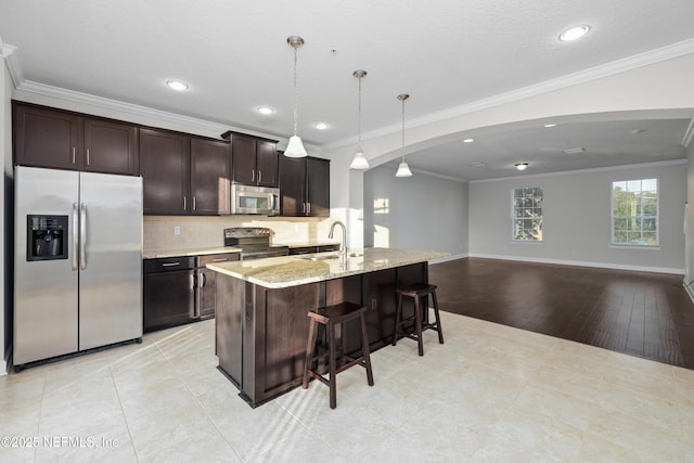 kitchen with a center island with sink, hanging light fixtures, light stone countertops, ornamental molding, and stainless steel appliances