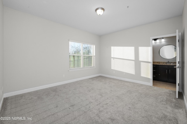 unfurnished bedroom featuring sink, light carpet, and ensuite bath