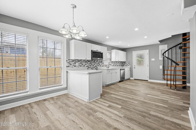 kitchen featuring light wood-type flooring, a wealth of natural light, stainless steel appliances, white cabinetry, and hanging light fixtures