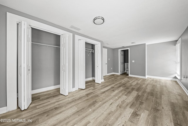 unfurnished bedroom featuring two closets and light hardwood / wood-style flooring