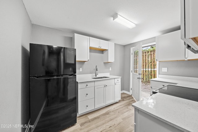 kitchen with light wood-type flooring, white cabinetry, black fridge, and sink